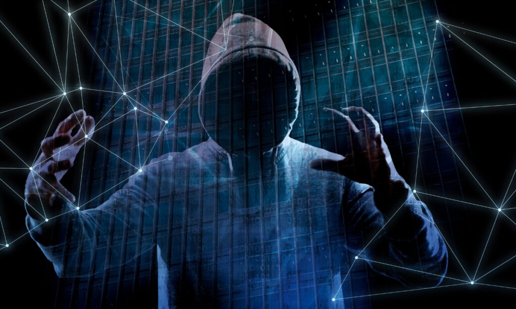 a person in a dark hoodie (used to represent a hacker) holding up their hands in a threatening manner