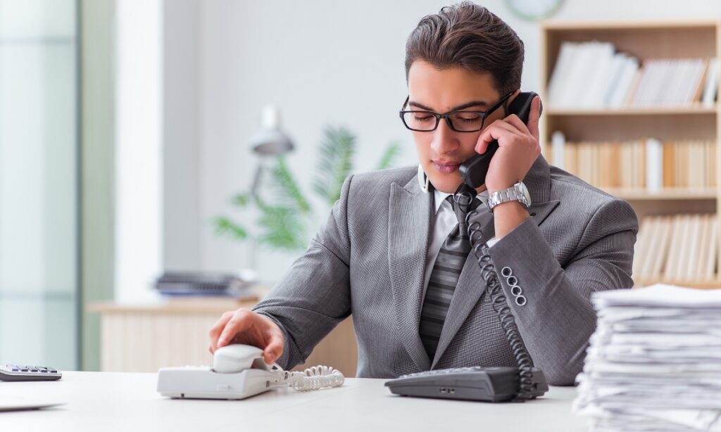 man in a suit holding one phone up to his ear while placing another back in the receiver