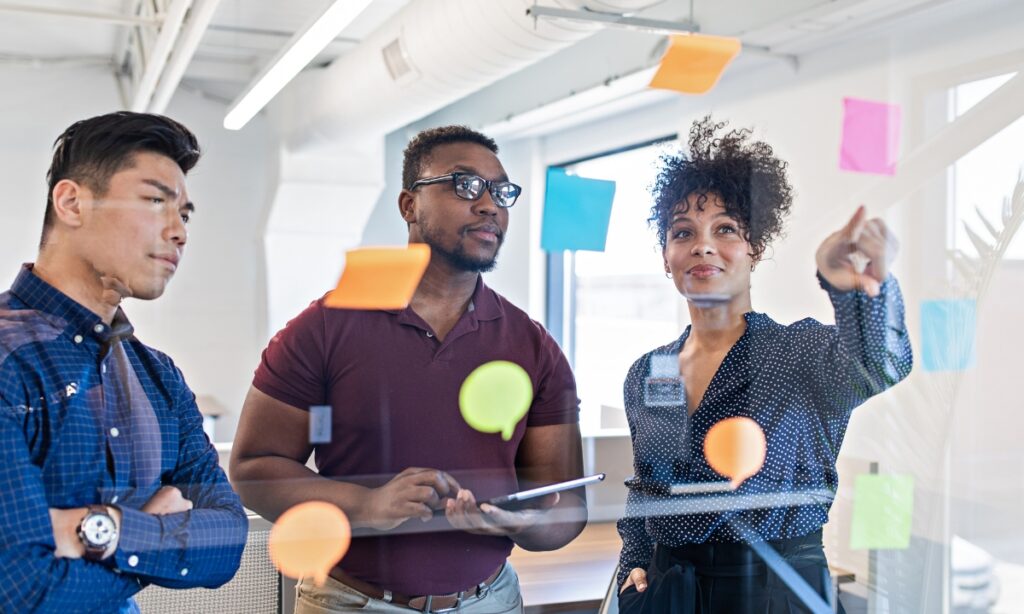 three people looking and pointing at a board covered in sticky notes