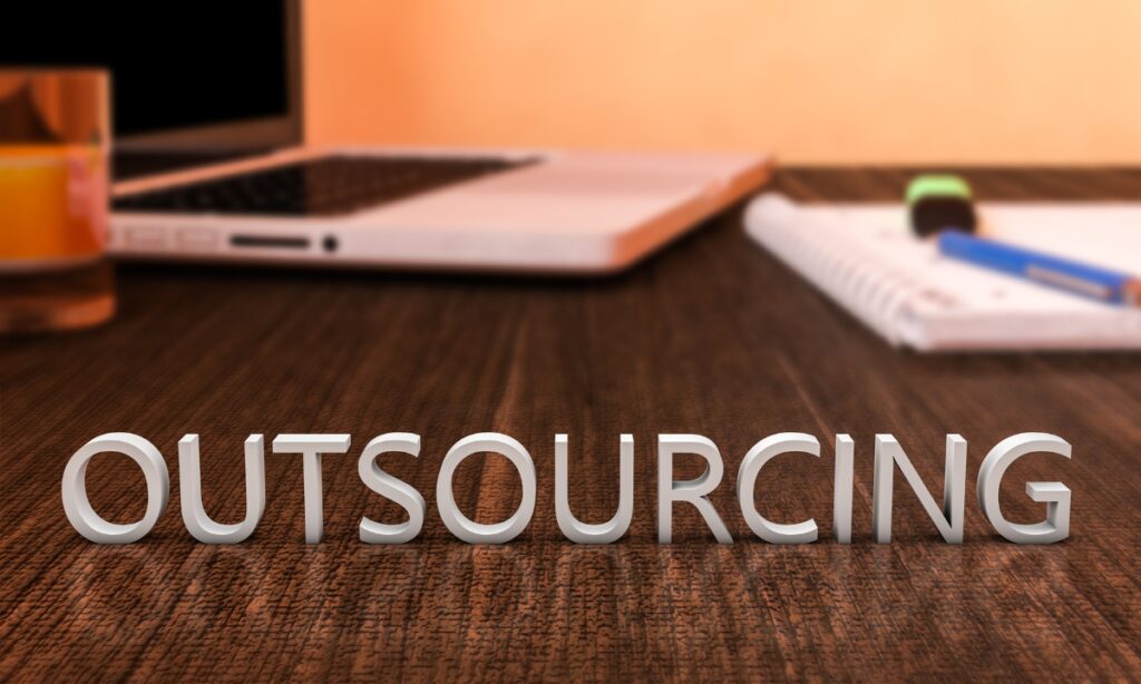 a dark wooden desk with blurry notebooks and the word "outsourcing" at the front