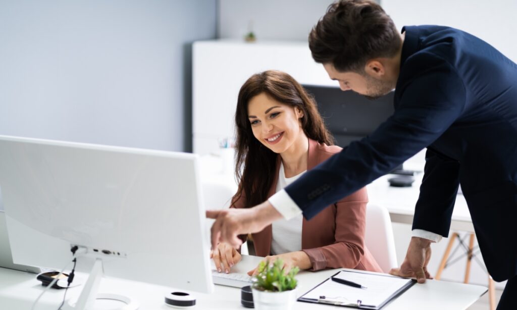 a man leaning near a woman to show her something on her computer screen in an office