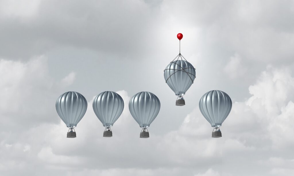 five silver hot air balloons lined up, but the fourth one has a small red balloon tied to the top, allowing it to float higher than the others, representing the advantage IT outsourcing offers