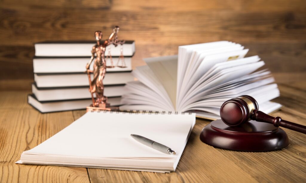 a stack of books, a notebook and pen, a lady justice statue, and a dark wooden gavel 