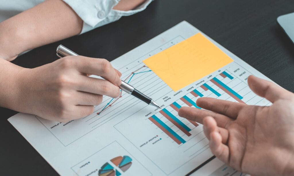 two people pointing at graphs on a wooden table