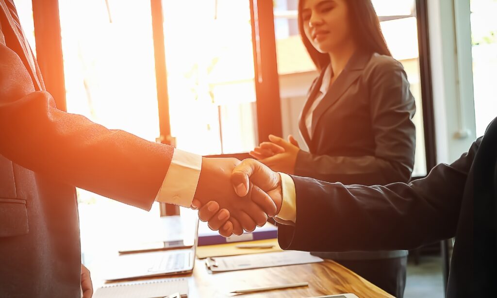 two people shaking hands in front of windows and a woman smiling at their clasped hands