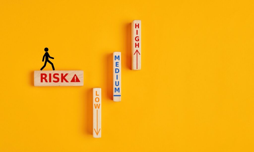 a stick figure standing on a wooden block that says "risk," with other wooden blocks that say "low," "medium," and "high" on them 