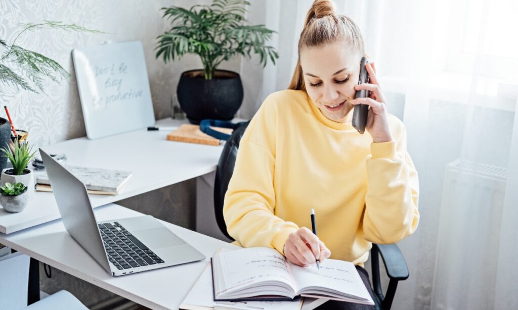 a woman on the phone writing in as notebook in her home office