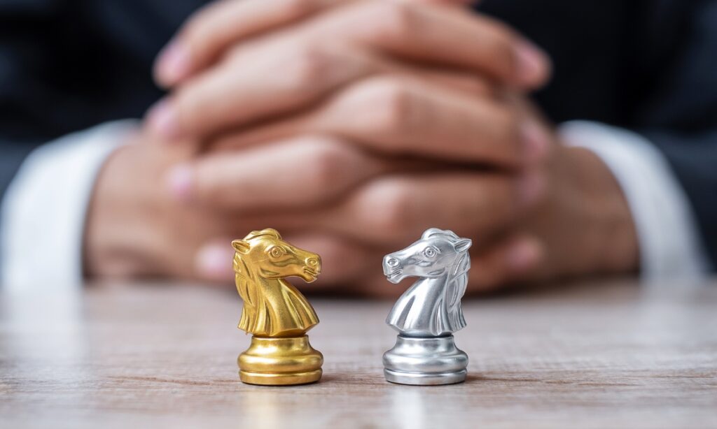 folded hands blurred out behind two chess knights; one is gold, and one is silver, used to signify communication services across barriers