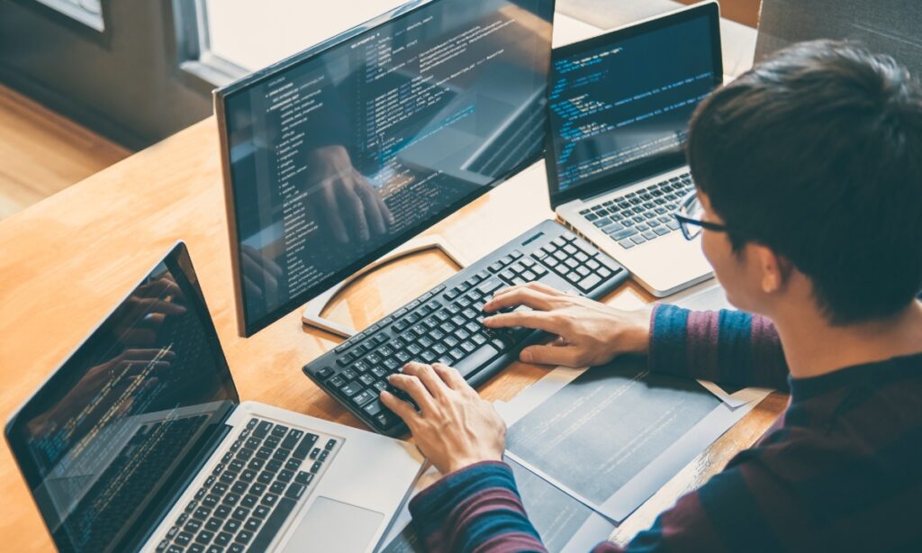 a man sits at a computer with laptops around him