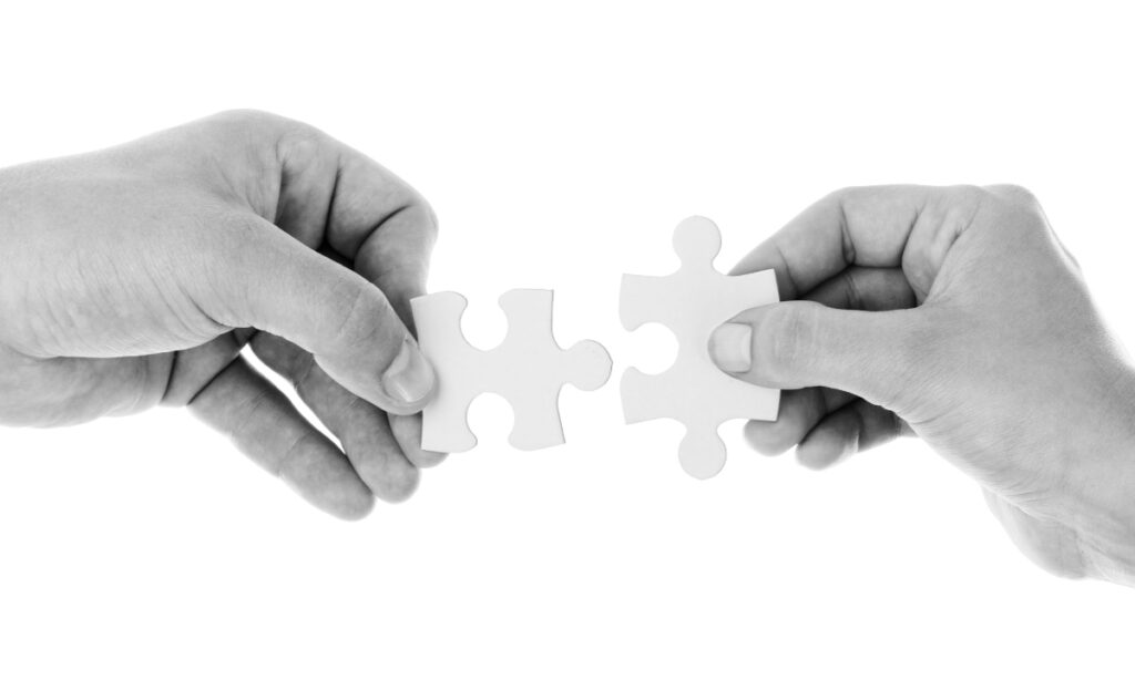 two people's hands holding up puzzle pieces to connect them