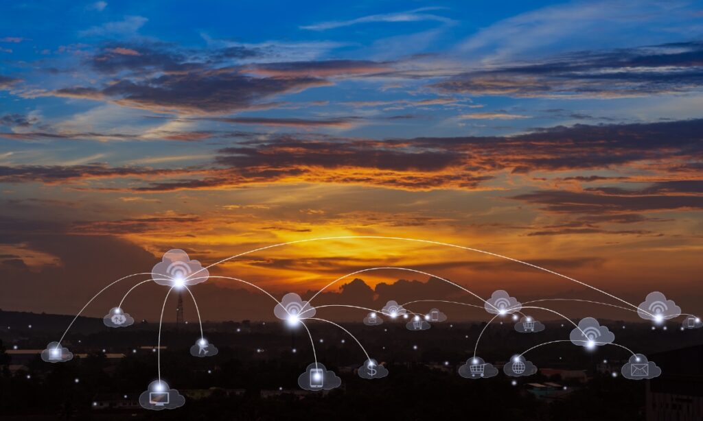 a skyline at sunset with small cloud icons and tendrils connecting the clouds to one another and to various buildings and device icons