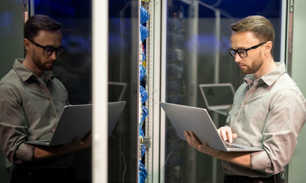 a man in a server room holding a laptop trying to fix a server