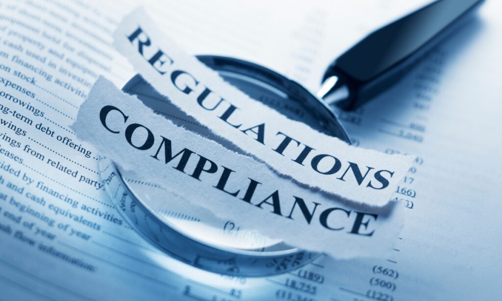 two pieces of paper on top of a magnifying glass and the pieces of paper read "regulations" and "compliance"