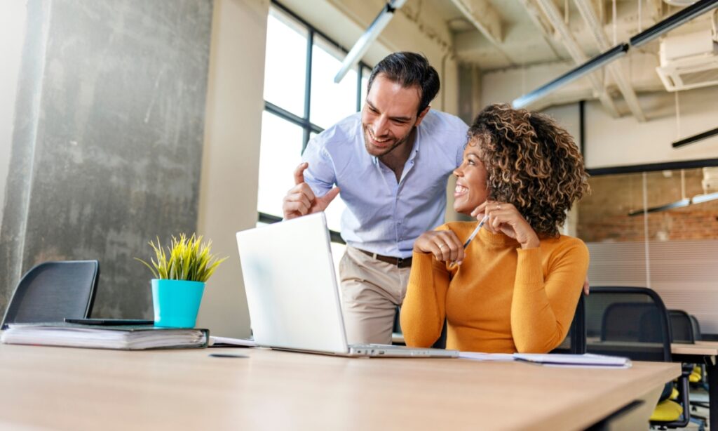 a man and a woman leaning over a laptop and smiling