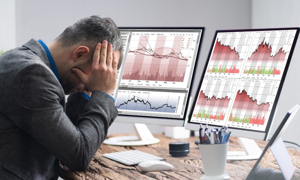 a man with his head in his hands while looking at charts on his computer