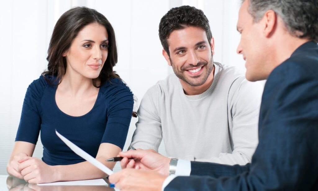 this picture seems like a couple speaking with a consultant; the consultant is holding a paper and pen, and the couple is smiling at him