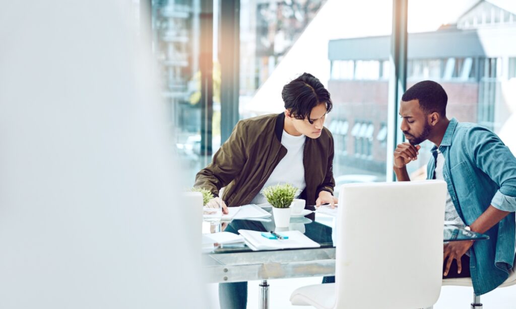 two men sitting at a table with paperwork and small plants scattered around it, presumably discussing managed IT services